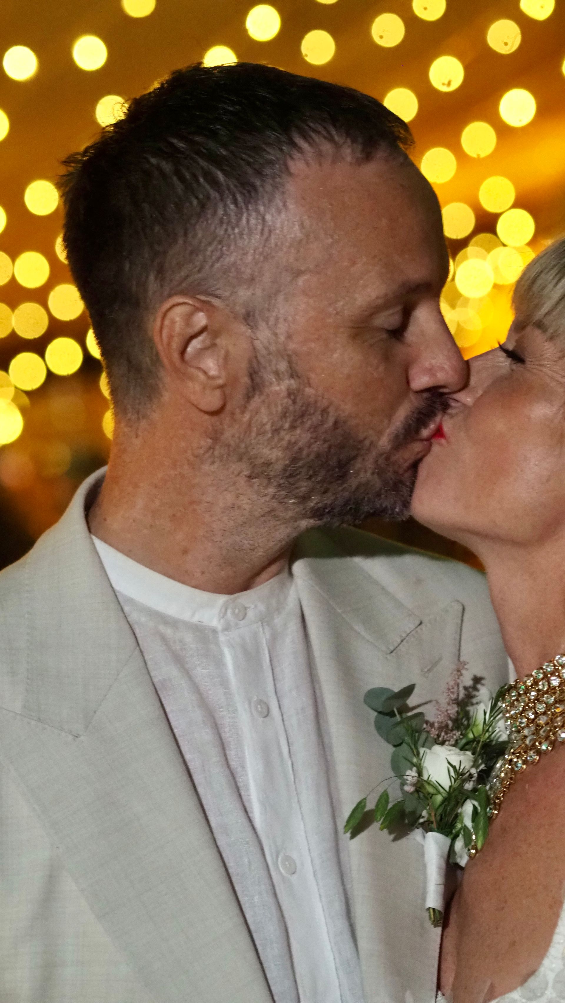 Couple kissing at a celebration, with warm golden lights in the background.