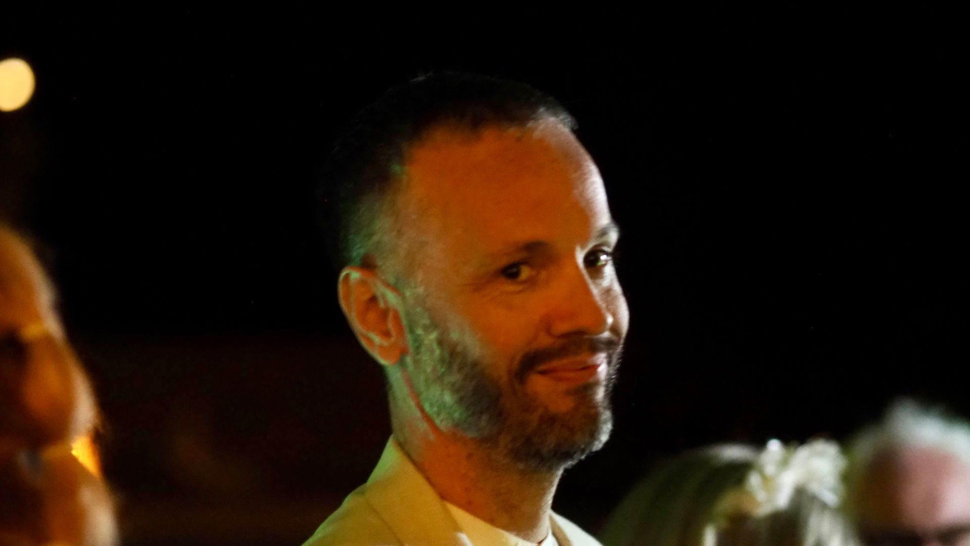 Man with a slight smile, lit by warm orange light against a dark background at an event