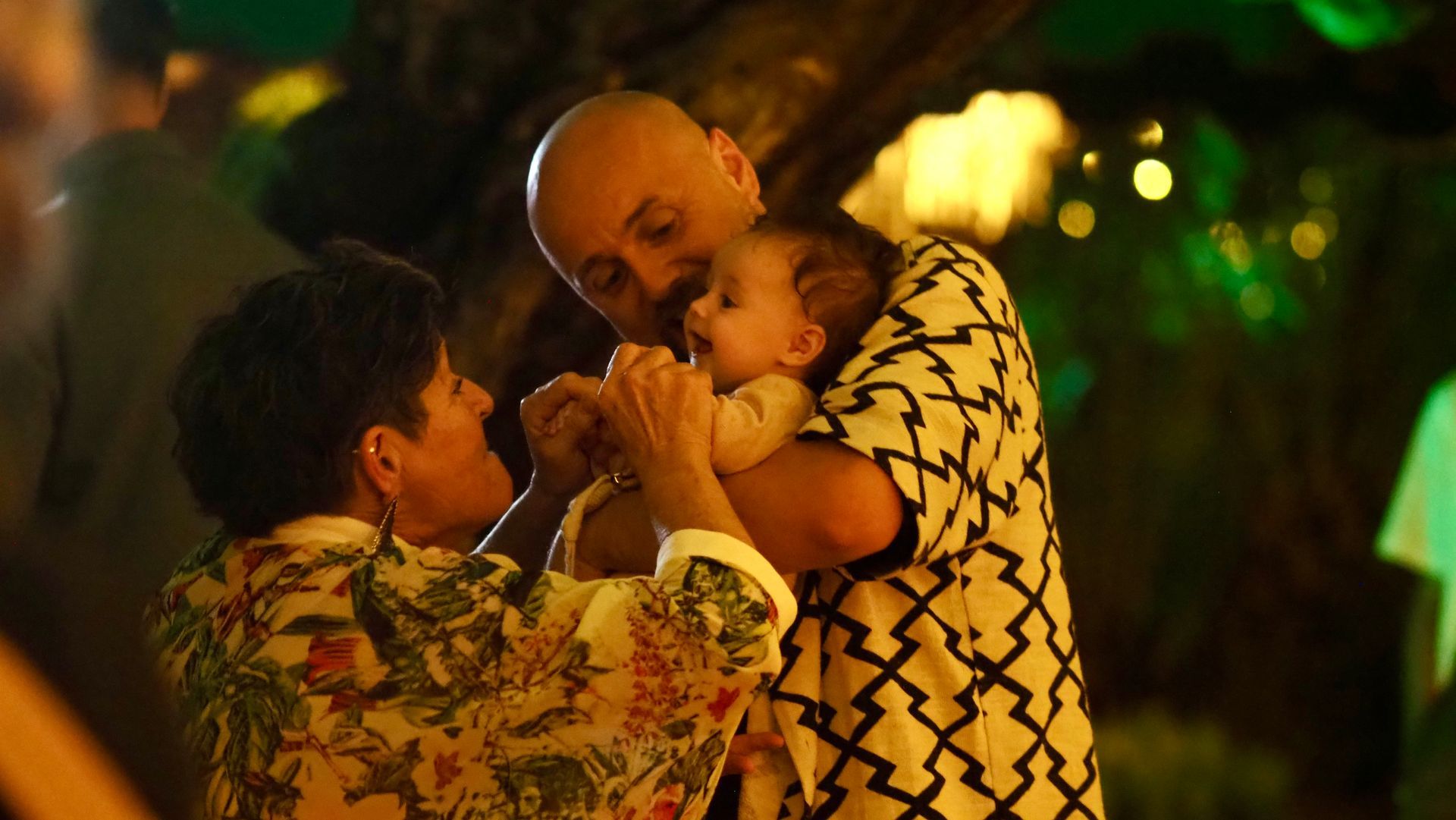 Two people holding and kissing a baby in a warm, softly lit outdoor setting