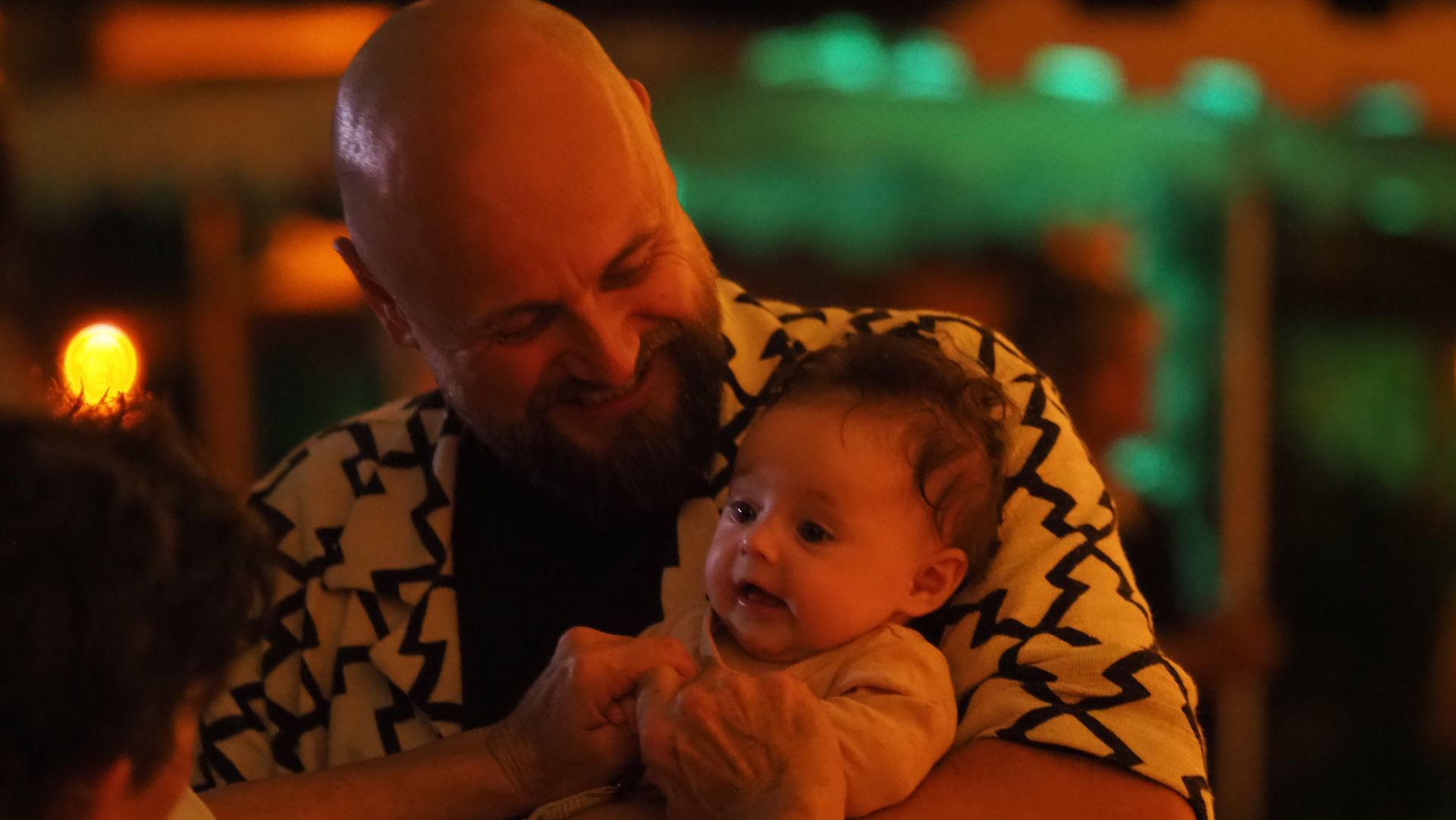 Man holding a baby in a warmly lit indoor setting, both looking at each other