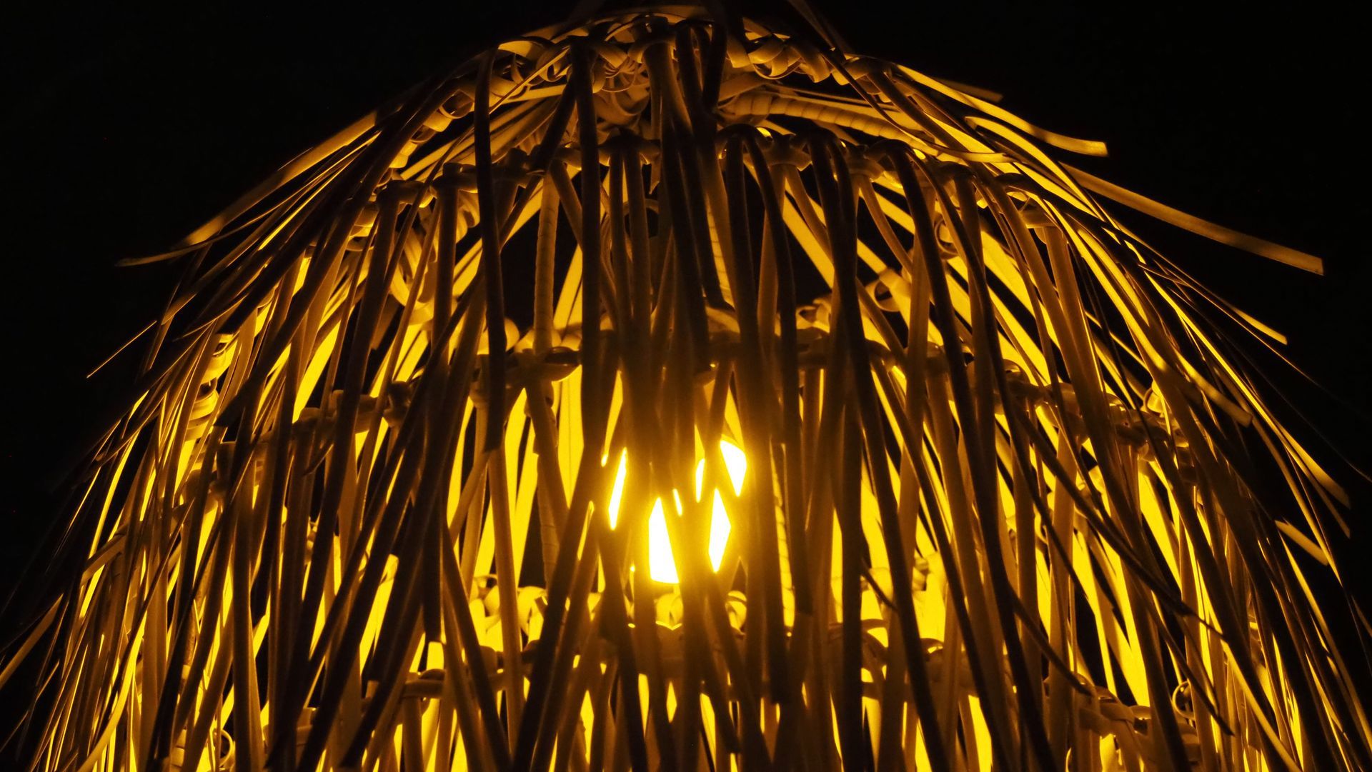 Warm yellow light glowing through a woven basket lamp shade in darkness