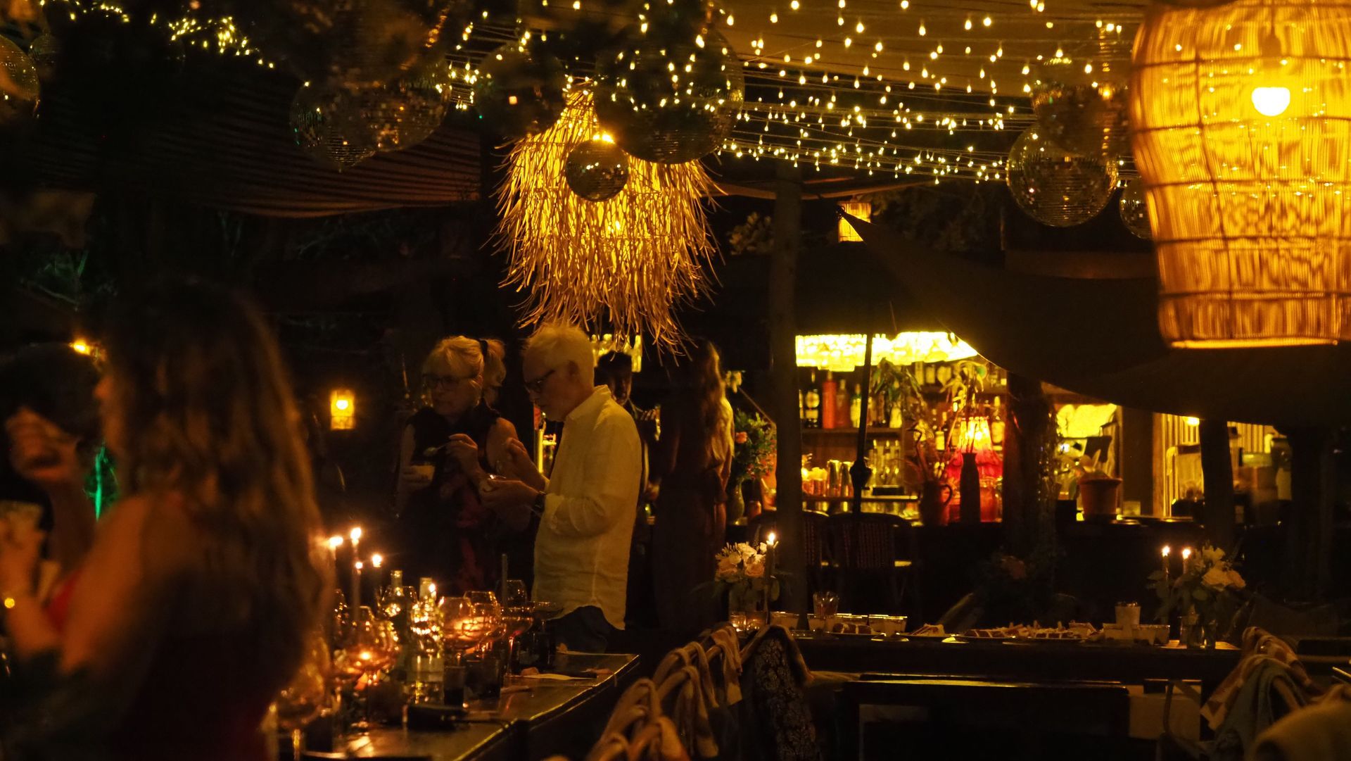 Dimly lit outdoor restaurant with warm string lights, hanging lanterns, and diners at tables at night