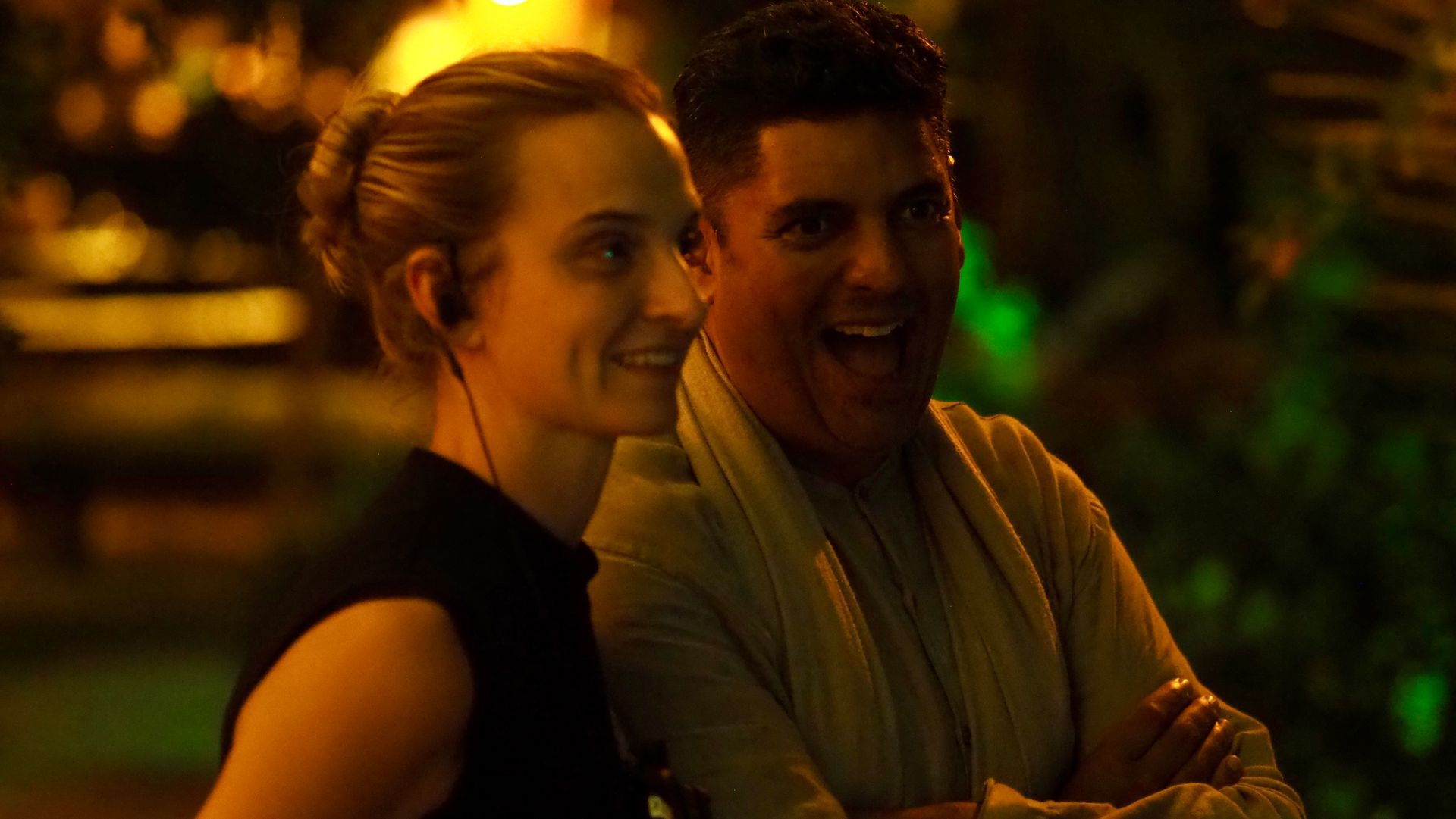 Two people smiling outdoors at night under warm orange lighting