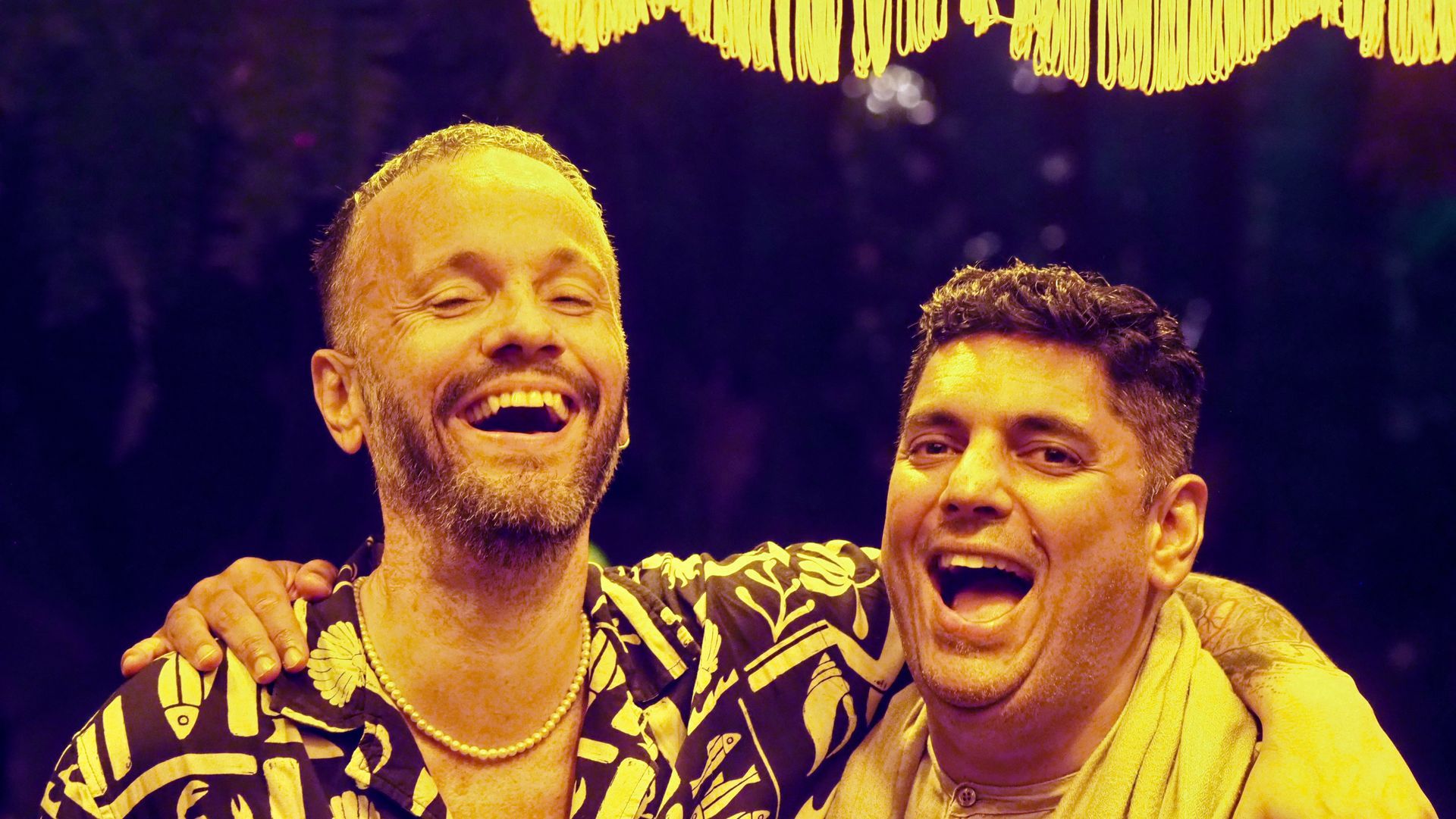 Two smiling men with arms around each other on a stage under purple and yellow lights.