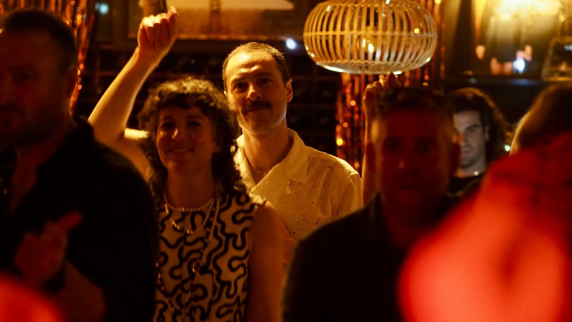 People dancing in warm orange club lighting, with one person smiling and raising an arm.
