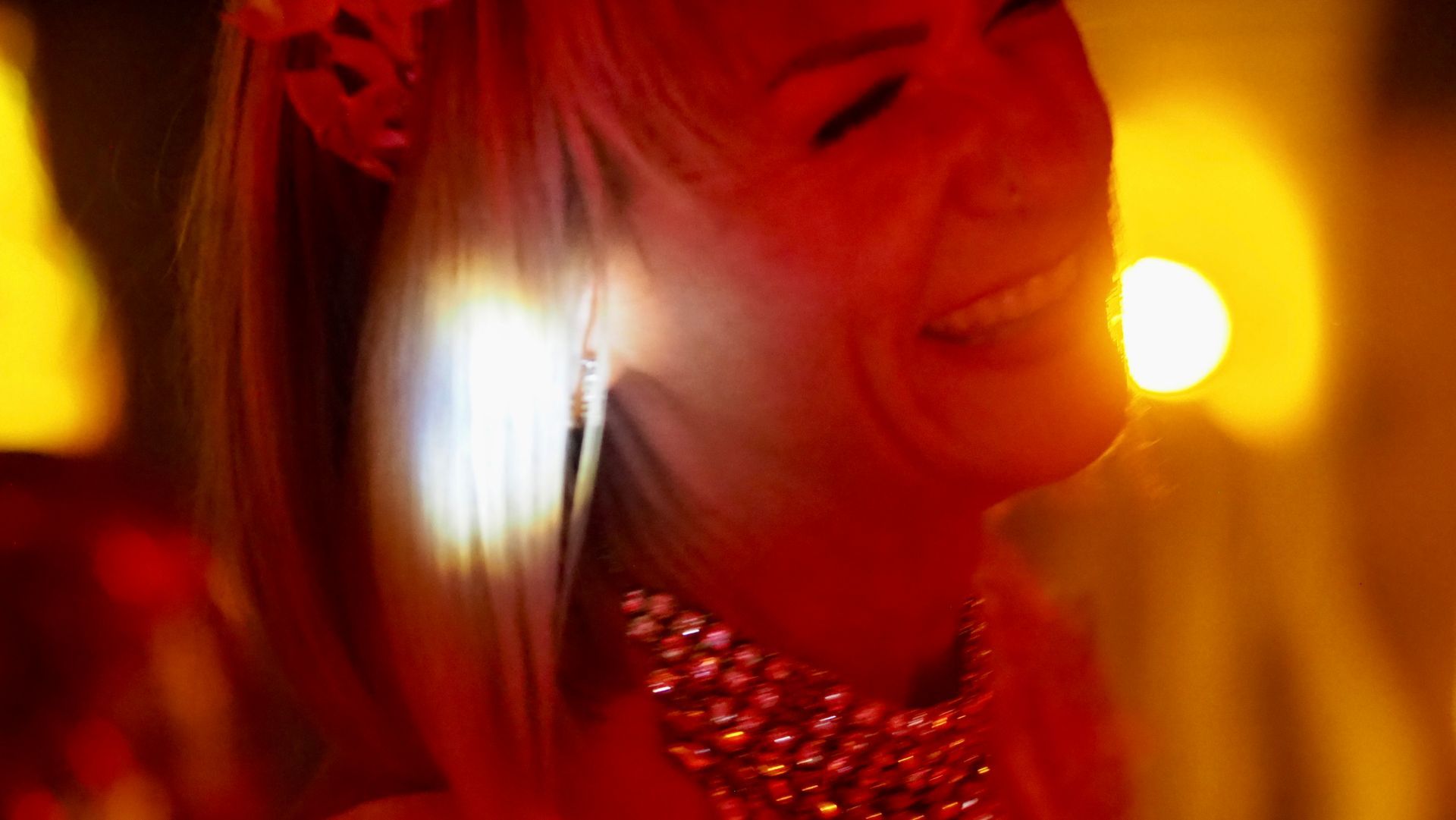 Smiling person in a red-lit close-up with bright bokeh lights in the background