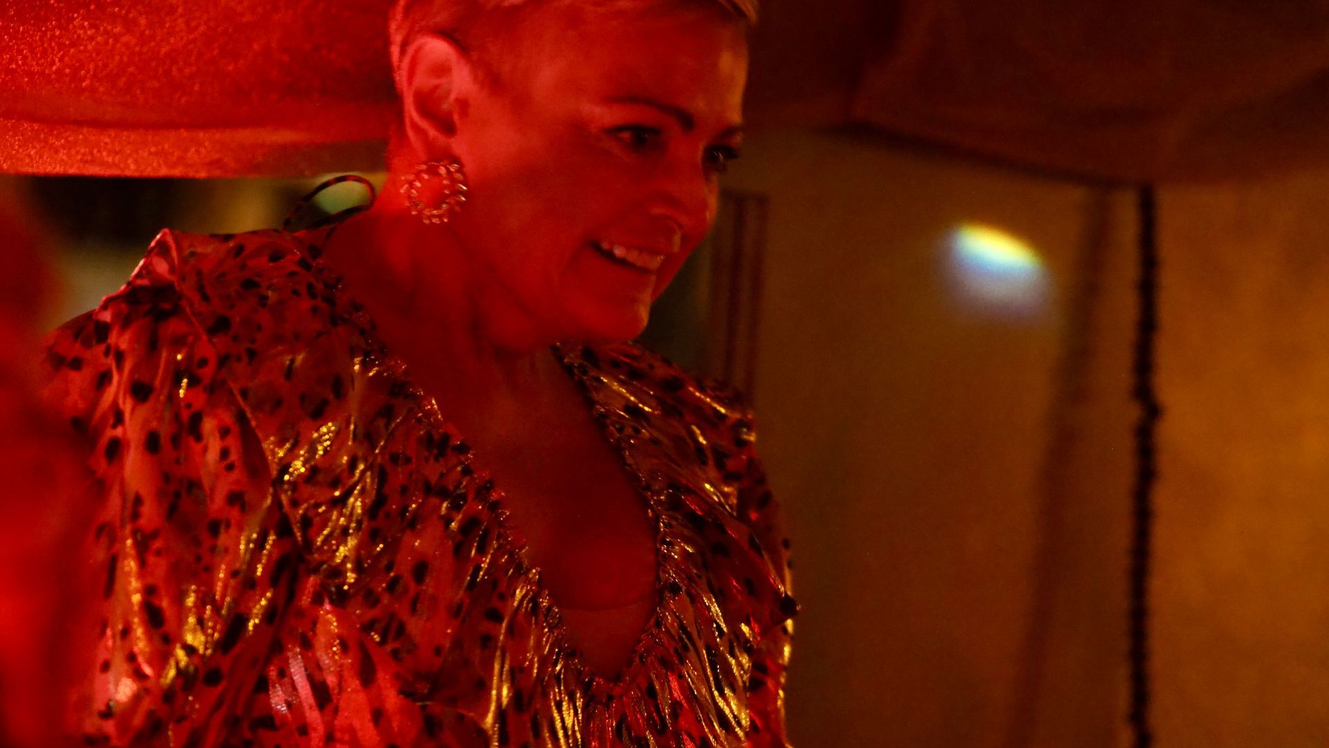 Person in a shimmering red outfit smiling under warm red lighting indoors