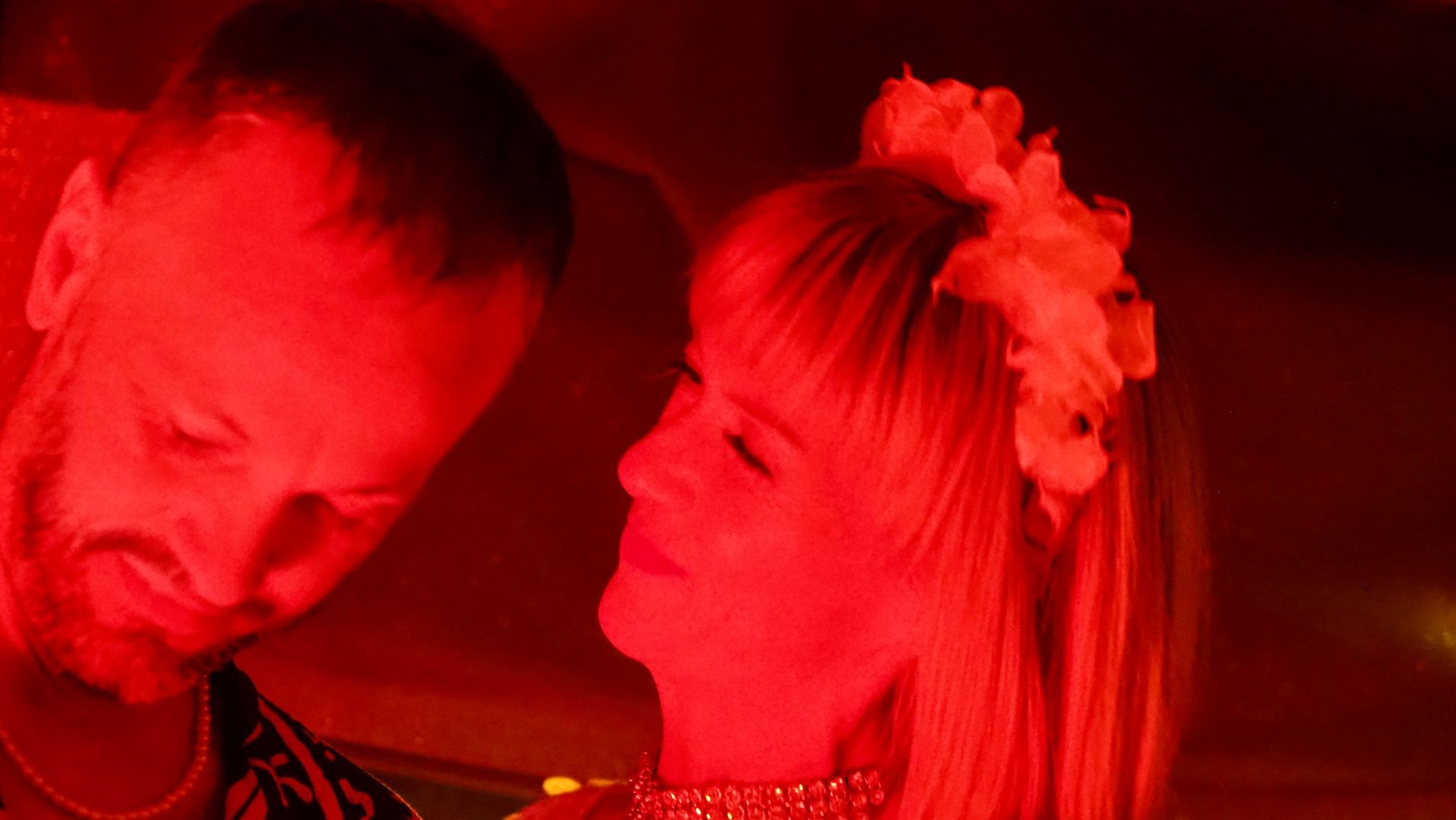 Two people under red lighting, smiling closely together at an event