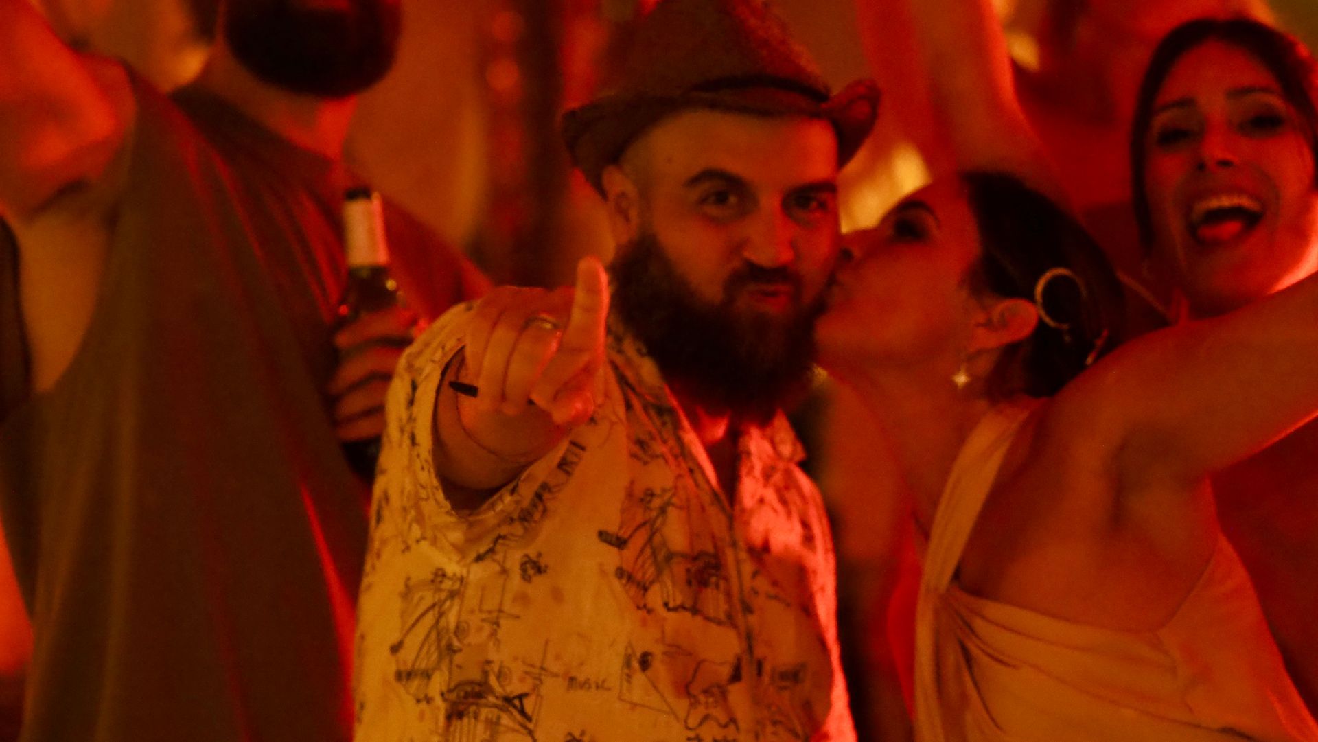 Bearded man pointing at camera amid a crowd in warm orange club lighting