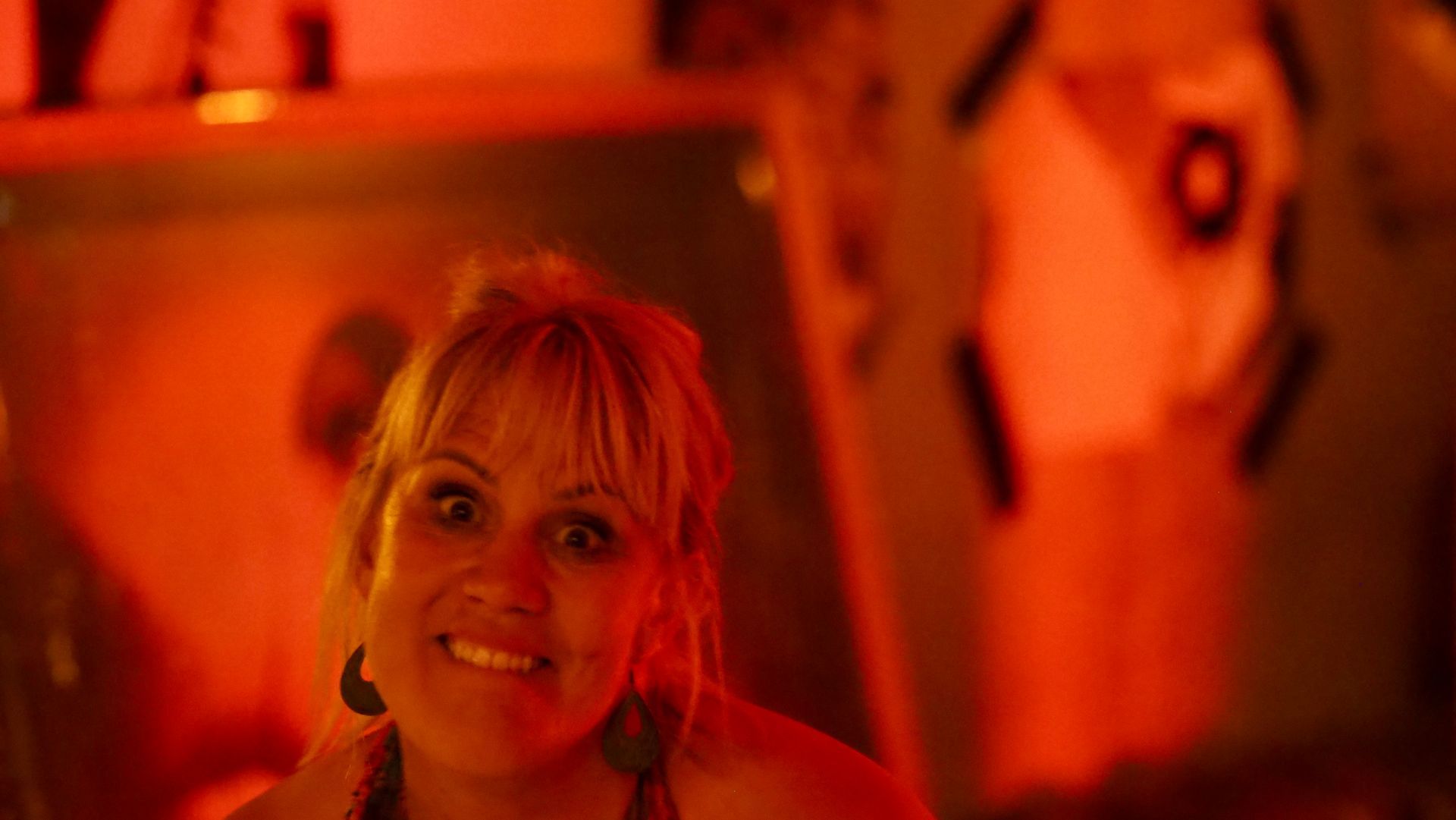 Smiling woman in warm orange-red lighting at a dimly lit event or bar