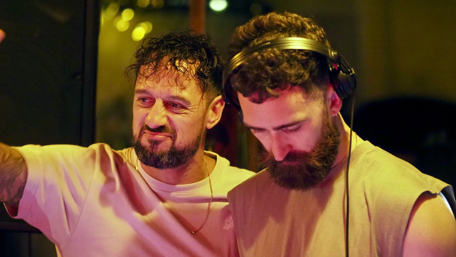 Two men in headphones DJing under warm pink and yellow lights