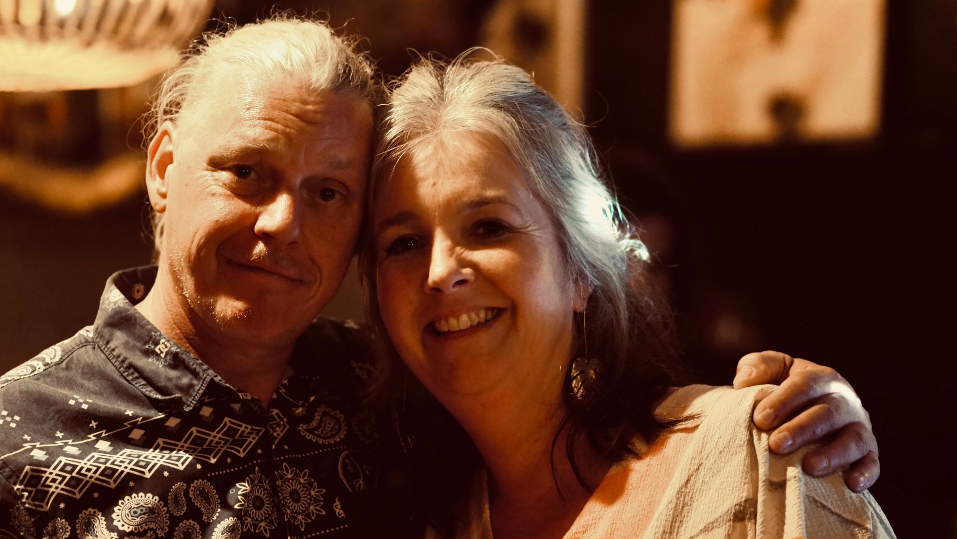 Two smiling adults posing closely together in warm indoor lighting