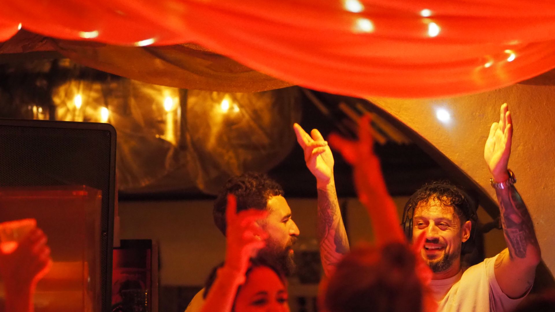People dancing under warm red lights at a lively indoor party, hands raised in celebration
