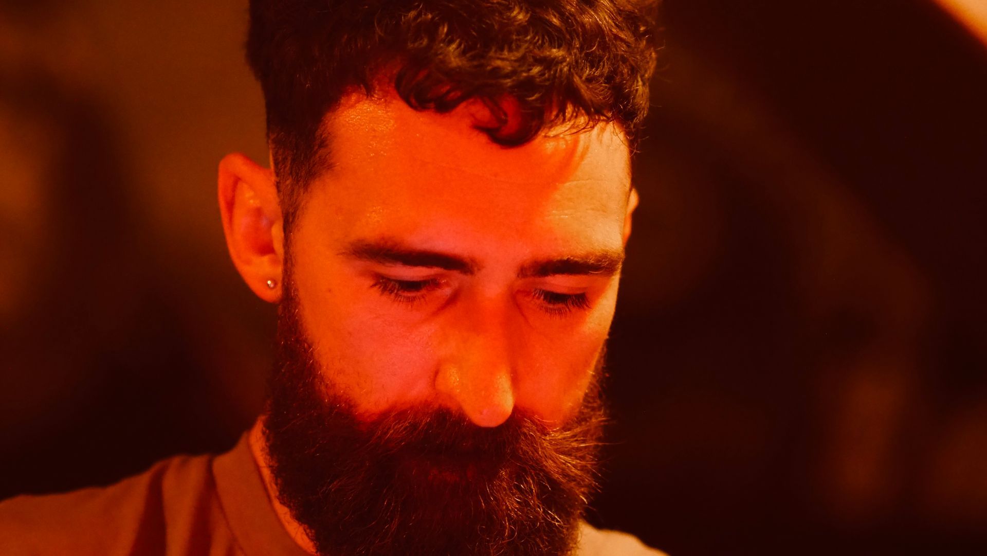 Close-up of a bearded man looking down under warm orange lighting