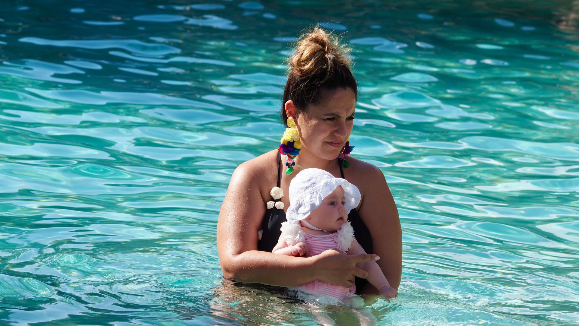 Woman holding a baby in turquoise water at a pool or beach