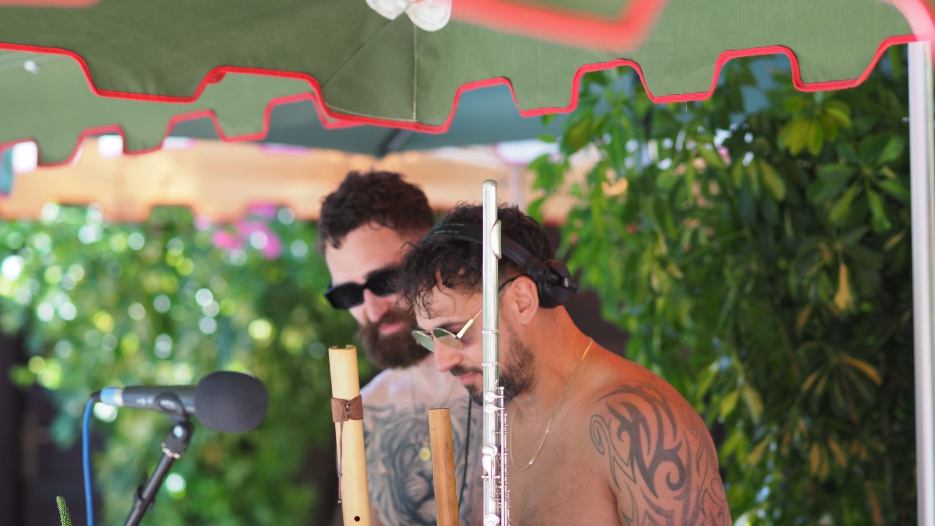 Two people in sunglasses standing under a canopy, with one speaking into a microphone outdoors.