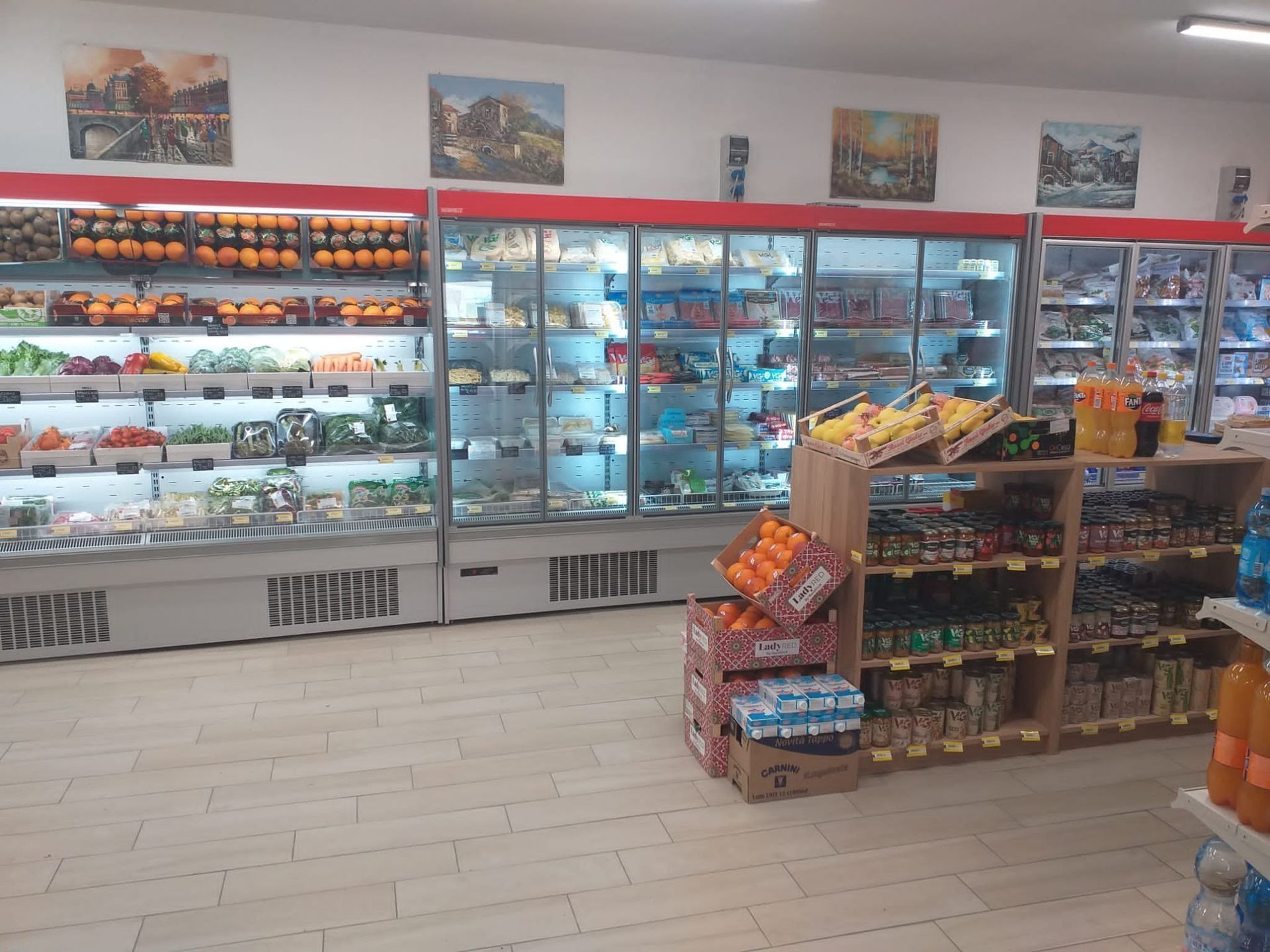 Una corsia di un supermercato con scaffali refrigerati riforniti di prodotti freschi e un espositore in legno con prodotti da dispensa.