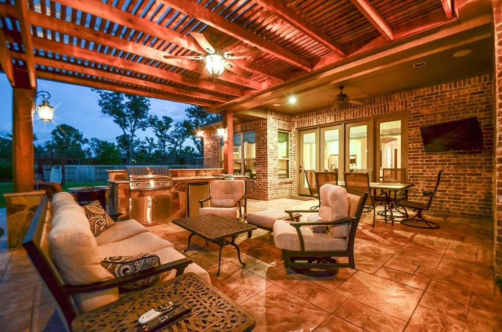 A cedar pergola patio with a couch , chairs , tables and a ceiling fan built in Katy, TX.