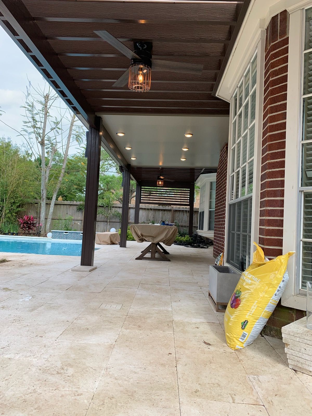 Installed shade structure with solid roof and two pergolas with recessed LED lighting and ceiling fans attached to a house in Richmond, TX.
