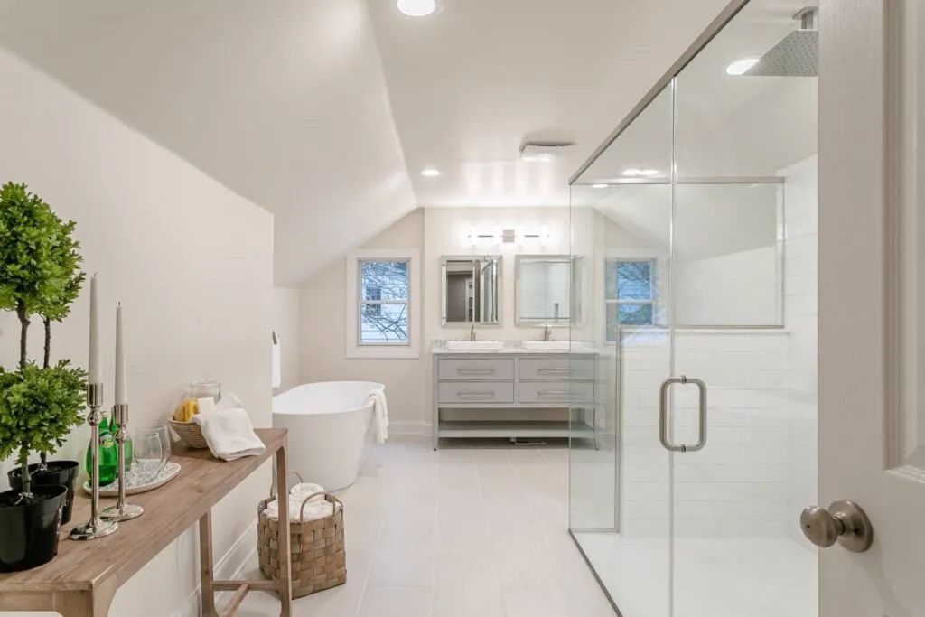 Bright modern bathroom with glass shower, vanity, freestanding tub, and potted plants