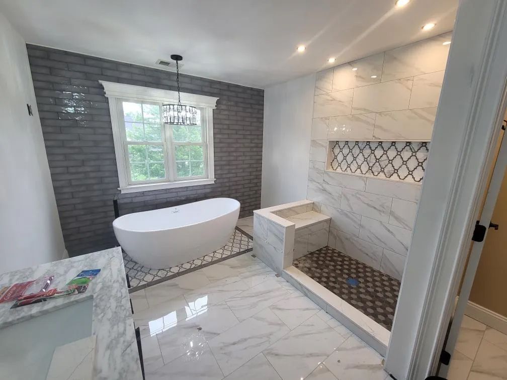Bright modern bathroom with freestanding tub, marble shower, and dark accent wall near a window