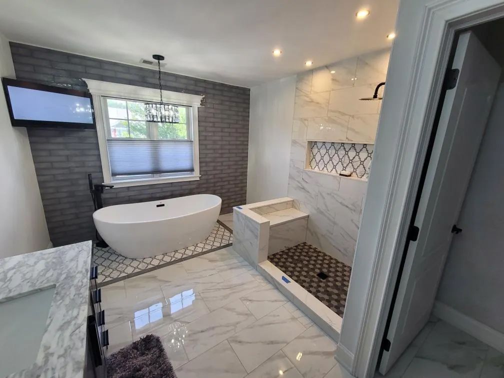 Modern luxury bathroom with a freestanding tub, marble tile, glass shower, and wall-mounted TV