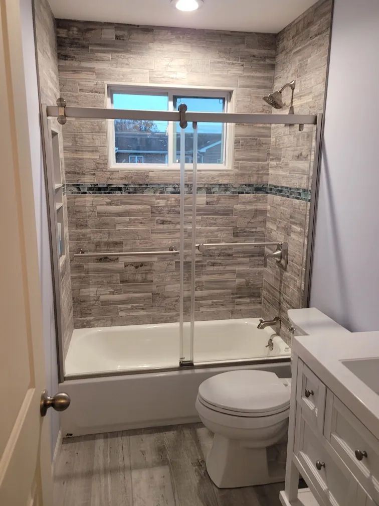 Small bathroom with tiled shower-tub, glass doors, toilet, and vanity.