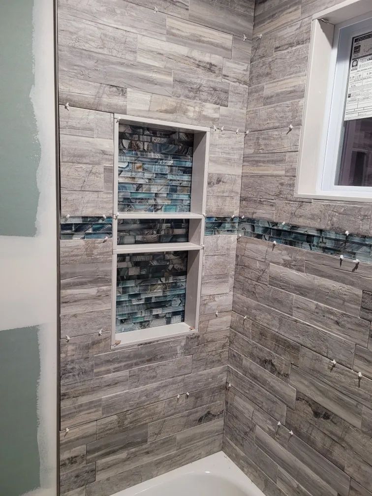 Tiled bathroom shower nook with a built-in recessed shelf and decorative mosaic accent strip