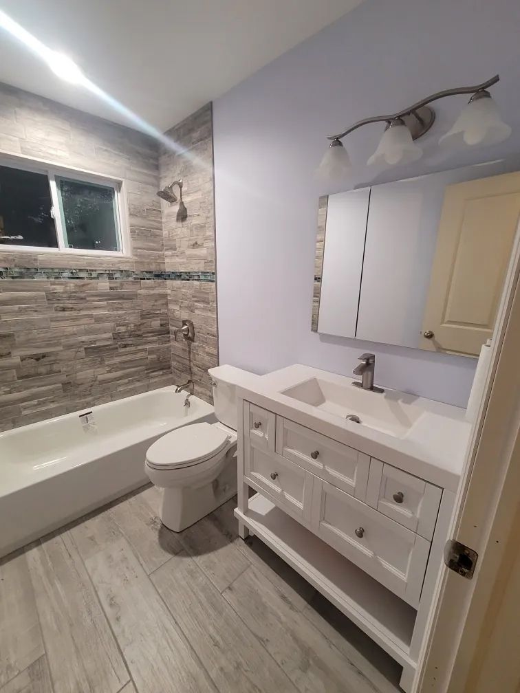 Bright bathroom with bathtub, toilet, and white vanity beside stone-tile shower wall.