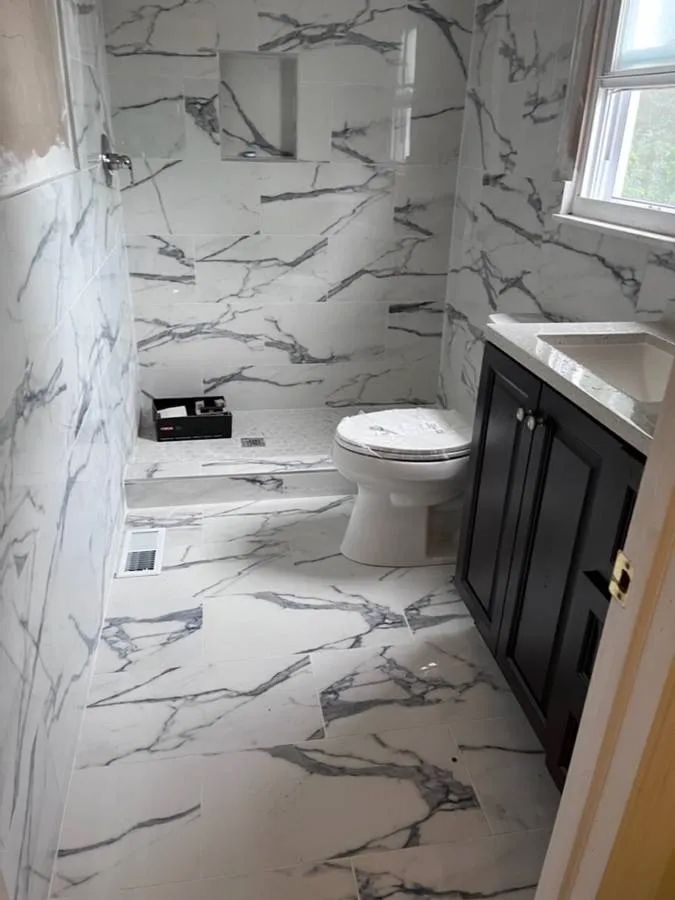 Small bathroom with marble-look tile, toilet, vanity, and window.