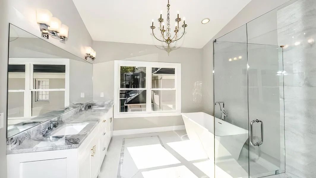 Bright white bathroom with double vanity, chandelier, large window, and glass walk-in shower