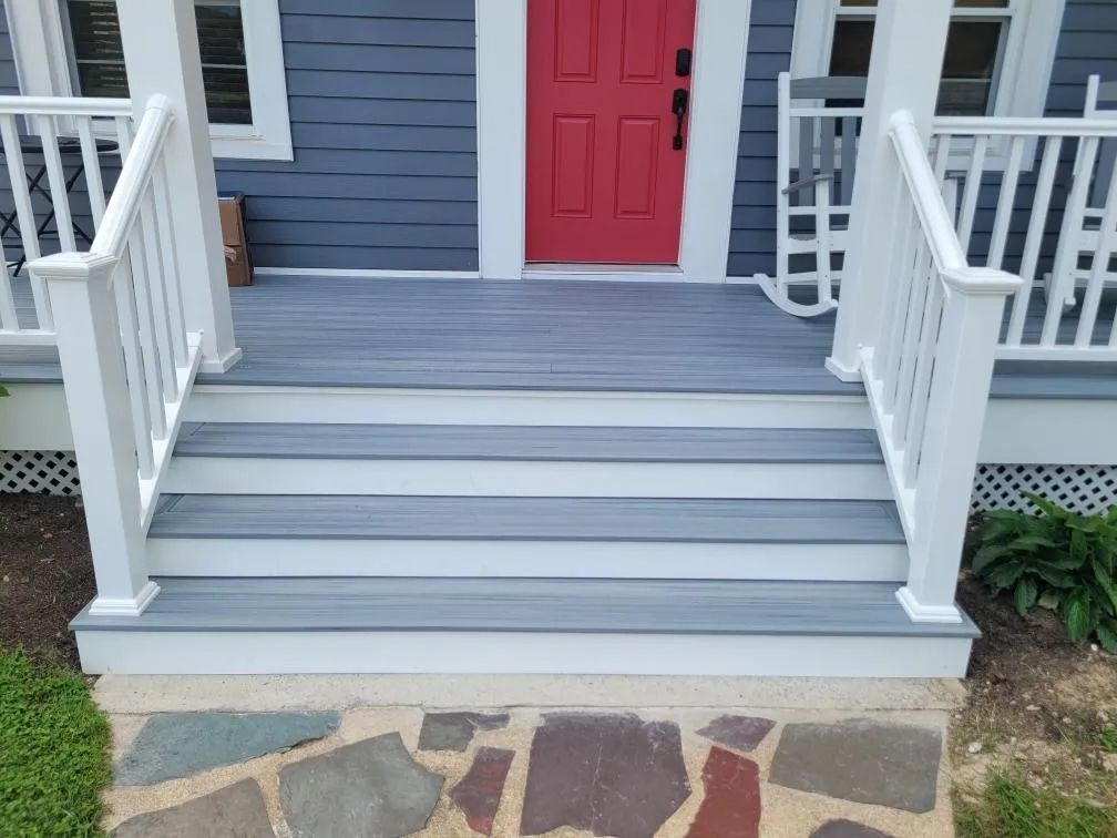 Front porch with gray steps, white railings, and a red front door above a stone walkway.