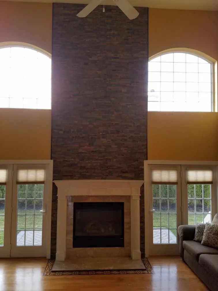 Living room with a central brick fireplace, tall windows, and high ceilings.