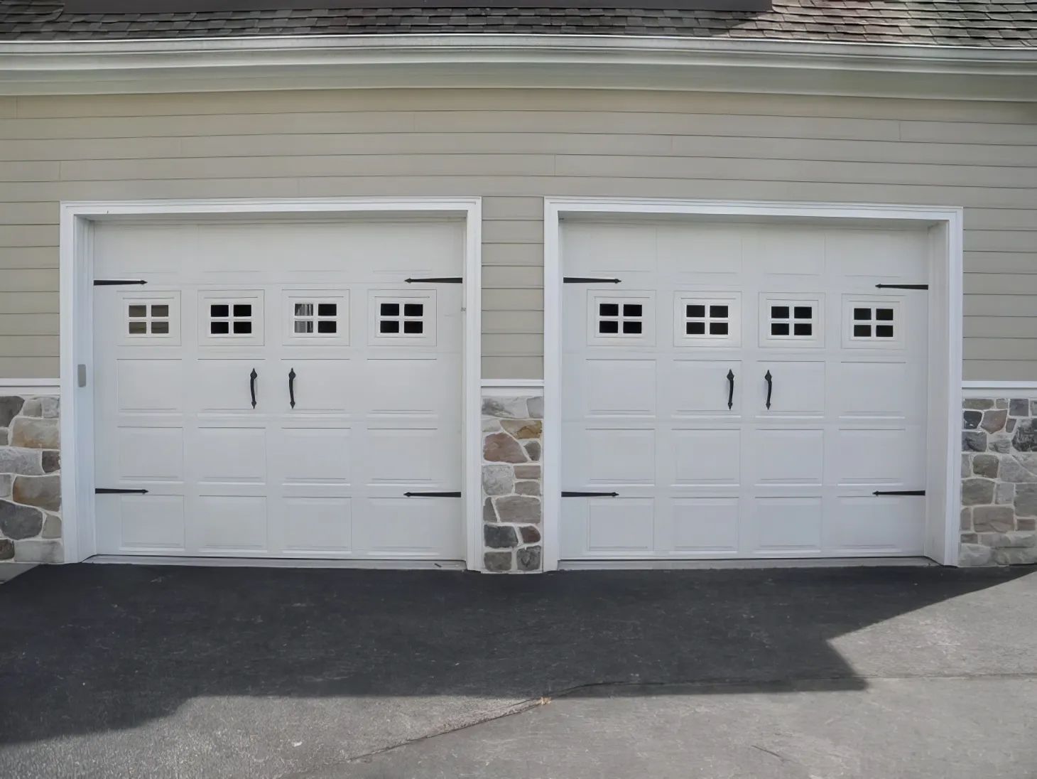 Two white garage doors in a beige siding building with stone accents and a dark driveway in front