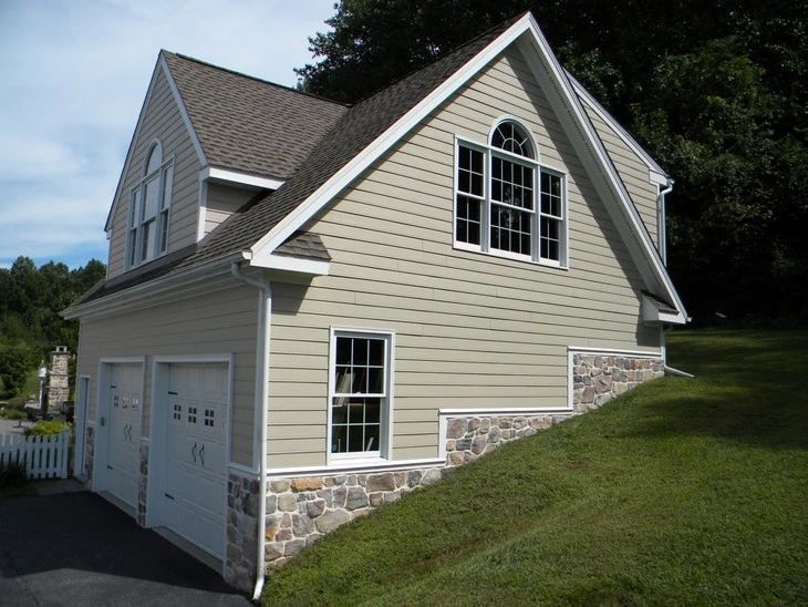 Beige house with stone foundation and double garage beside a grassy slope