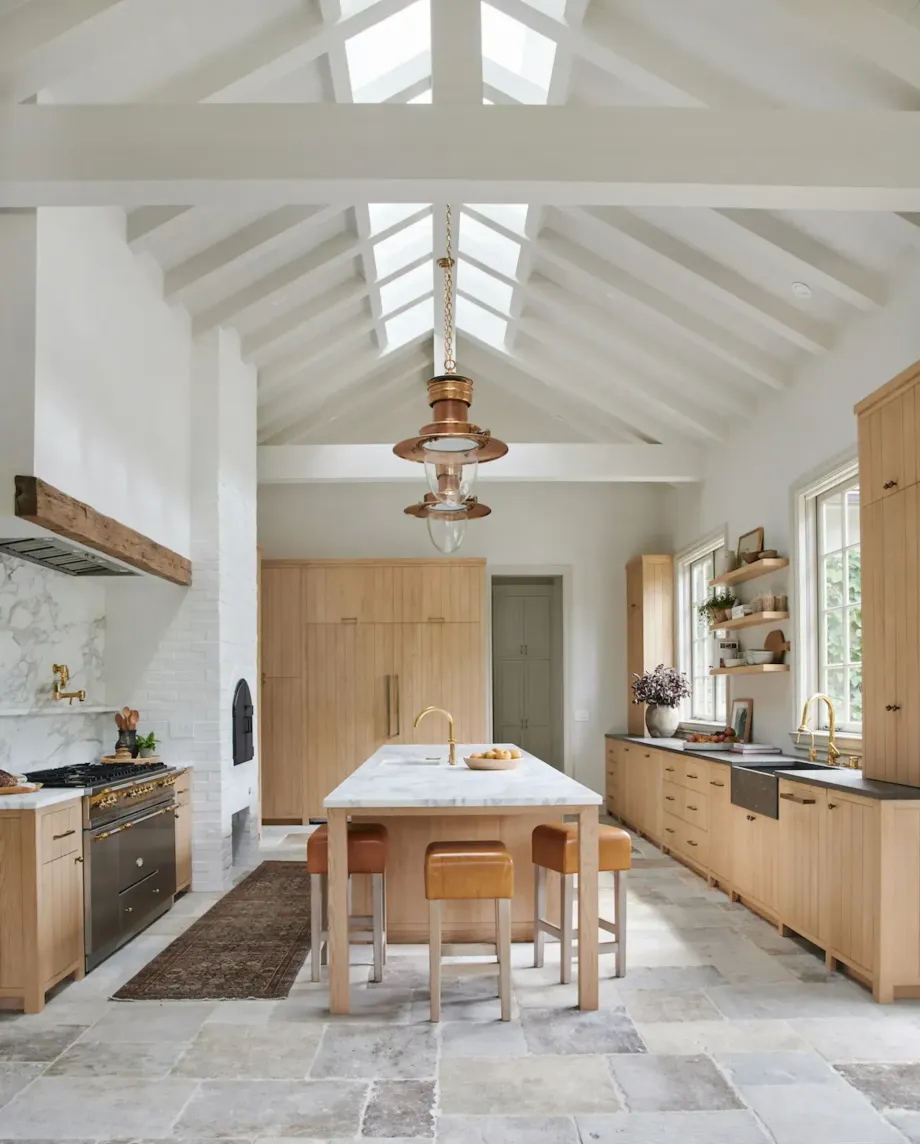 Bright modern kitchen with a long wooden table, skylights, and light wood cabinetry
