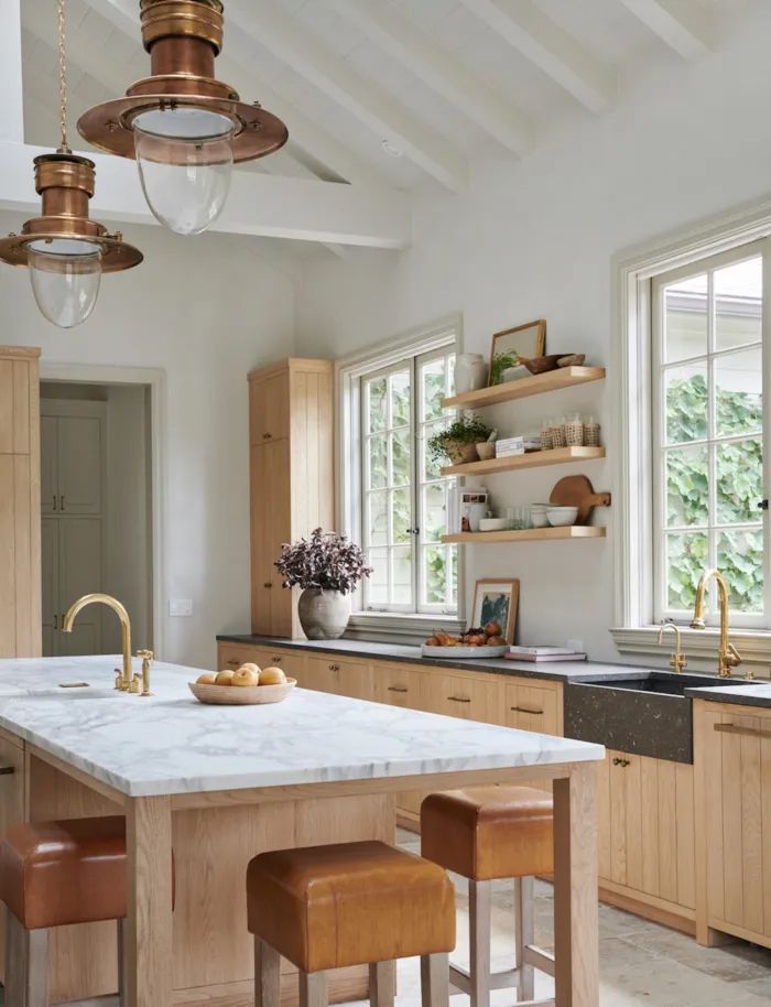 Bright modern kitchen with white island, wood cabinetry, open shelves, and pendant lights by large windows
