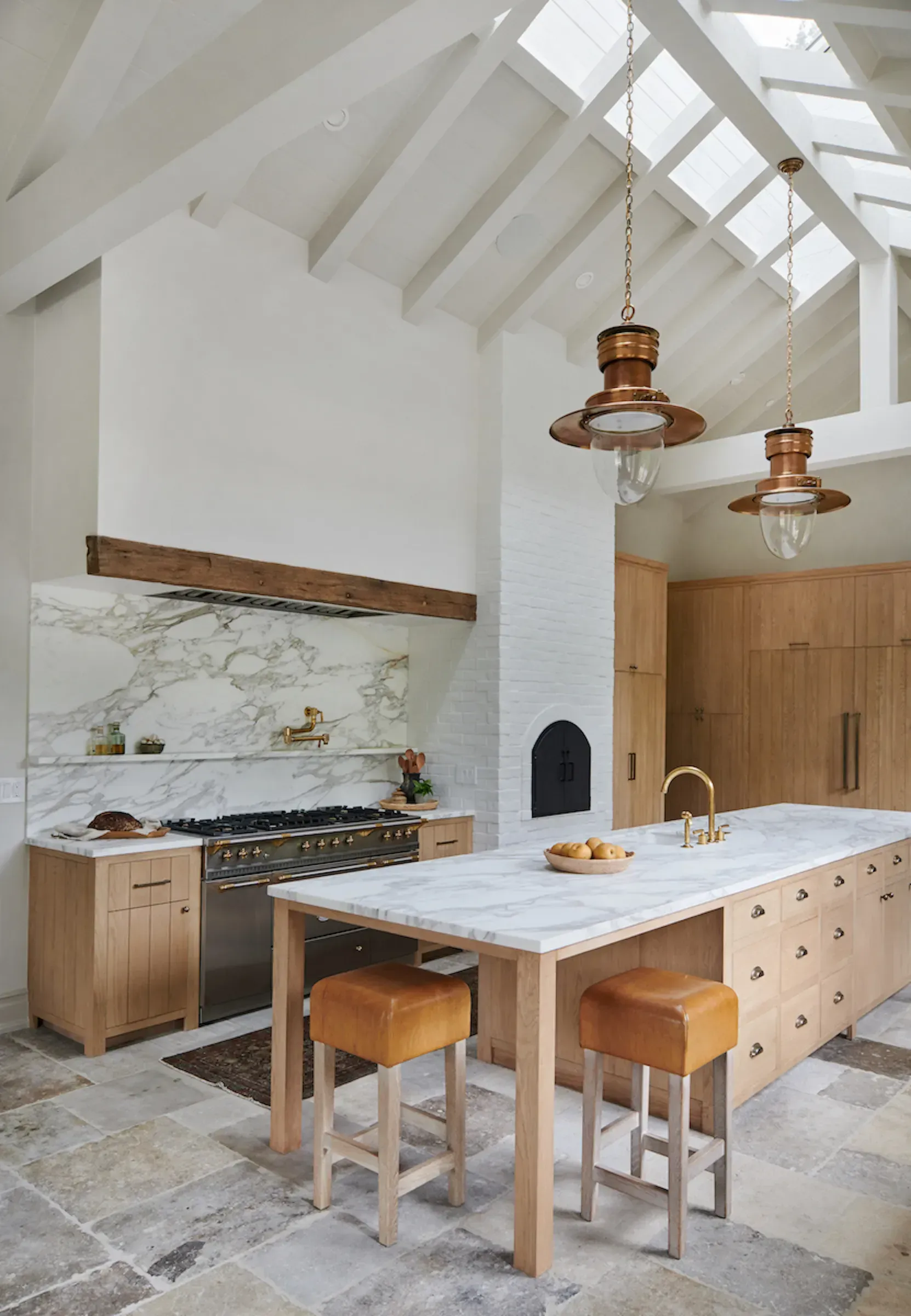 Bright modern kitchen with white vaulted ceiling, marble island, wood cabinets, and hanging pendant lights