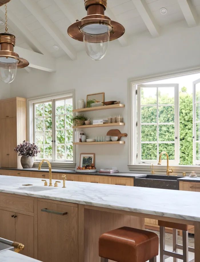 Bright kitchen with white countertops, wood cabinets, large windows, and open shelves, lit by hanging pendant lights