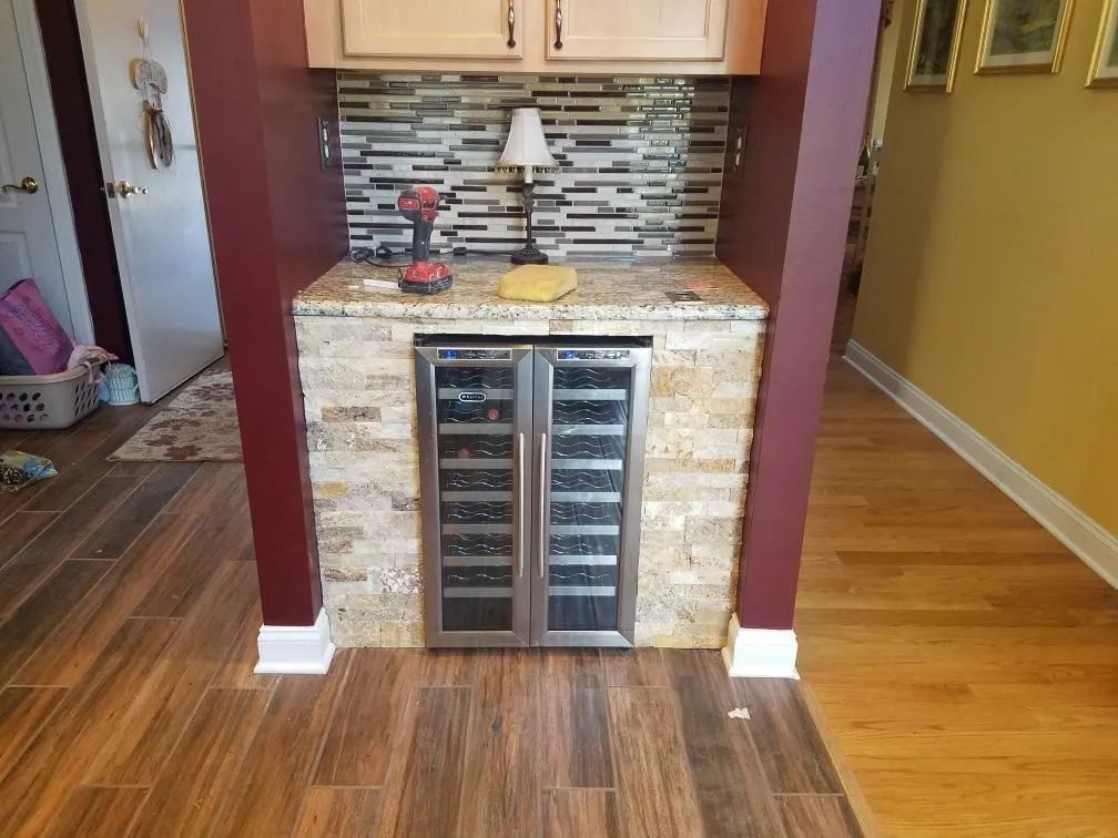 Compact home wet bar with granite countertop, wine cooler, and mosaic tile backsplash between burgundy walls