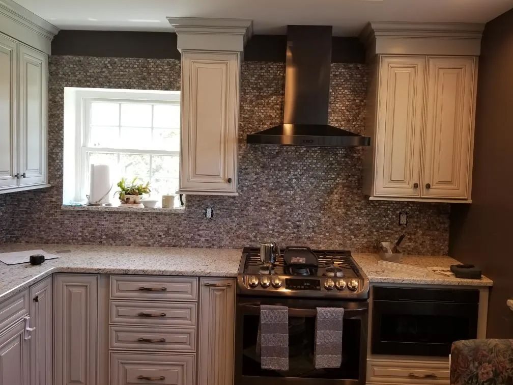 Modern kitchen with cream cabinets, mosaic backsplash, window, and stainless steel stove and hood