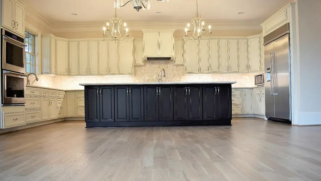 Spacious modern kitchen with dark island, white cabinets, light wood floors, and stainless steel appliances