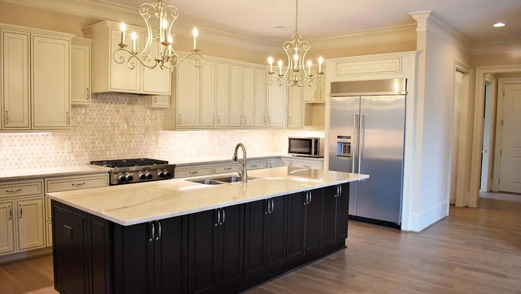Bright modern kitchen with white cabinets, dark island, marble countertops, and stainless steel appliances
