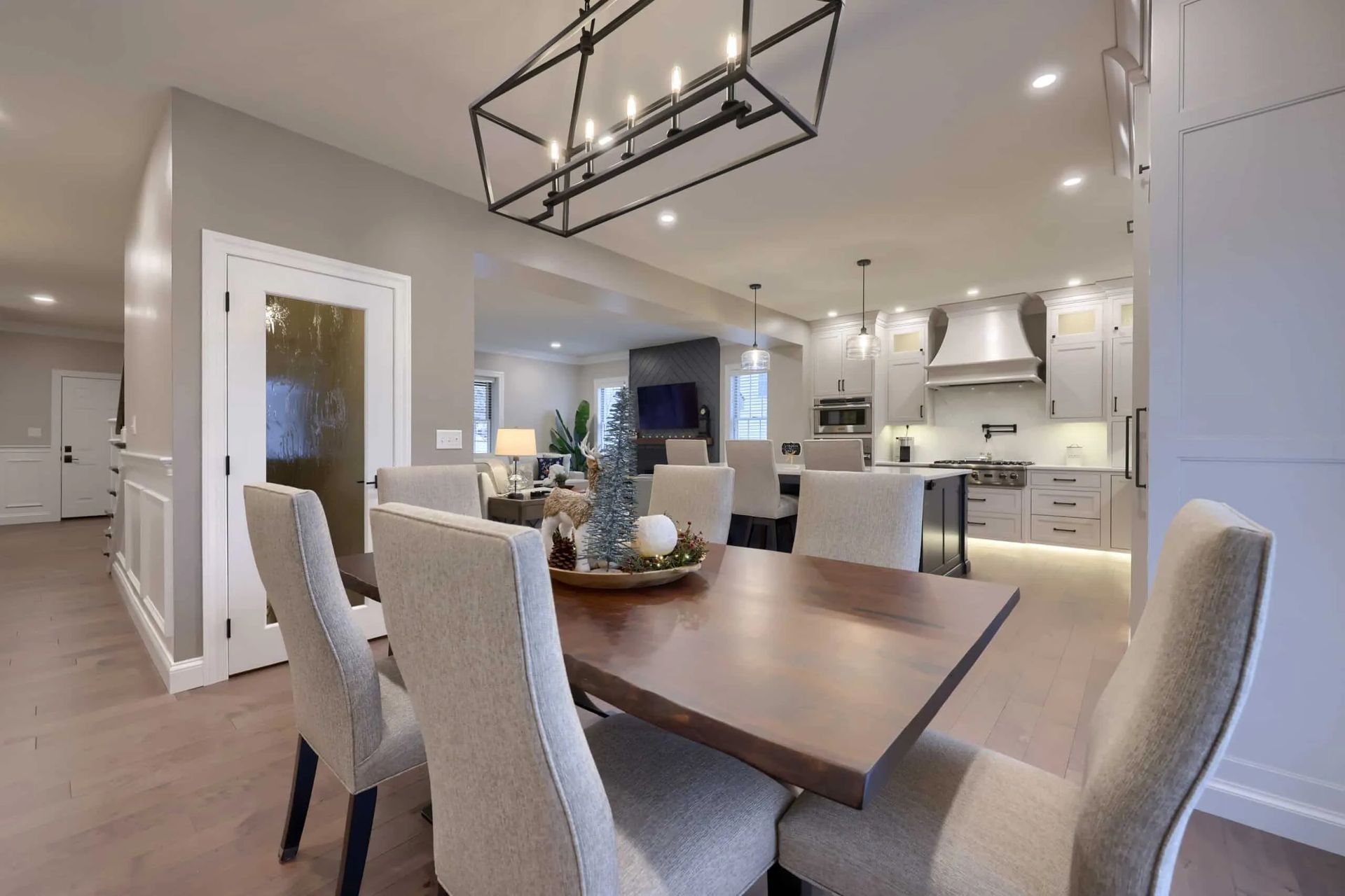 Modern open-concept dining and kitchen area with wood table, upholstered chairs, and white cabinets