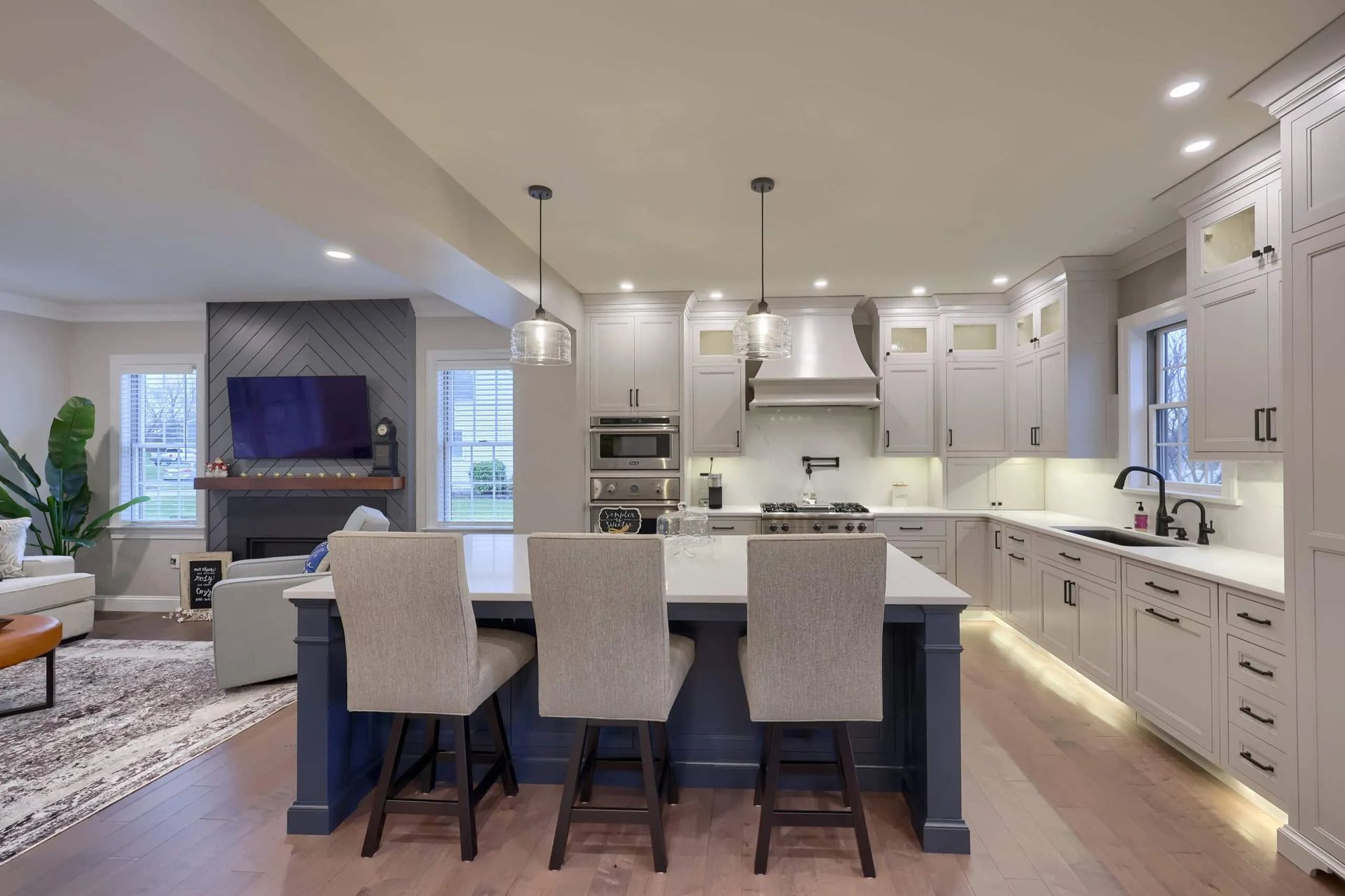 Bright open-plan kitchen with island seating, white cabinets, and living room in the background