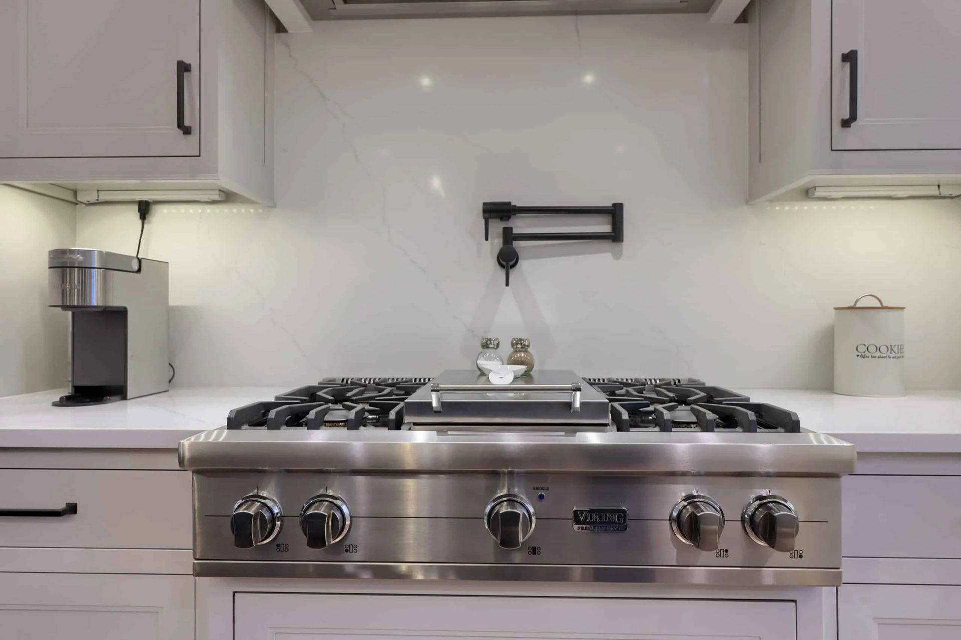 Modern white kitchen with a stainless steel gas range and built-in coffee maker on the counter