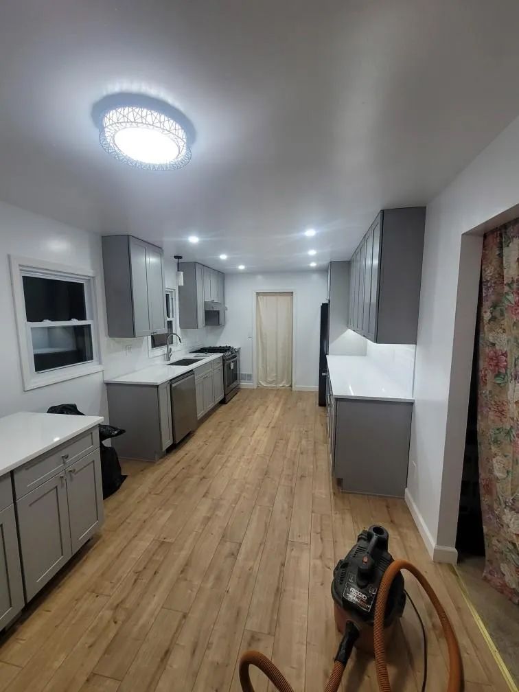 Bright modern galley kitchen with gray cabinets, wood floor, white island, and ceiling lights