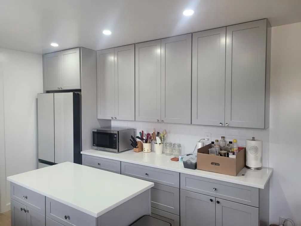 Modern kitchen with gray cabinets, white counters, island, microwave, and a refrigerator