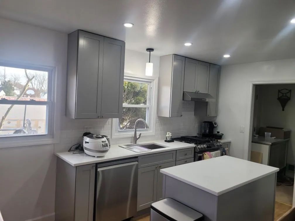 Modern kitchen with gray cabinets, white countertops, island, stainless dishwasher, and large window.