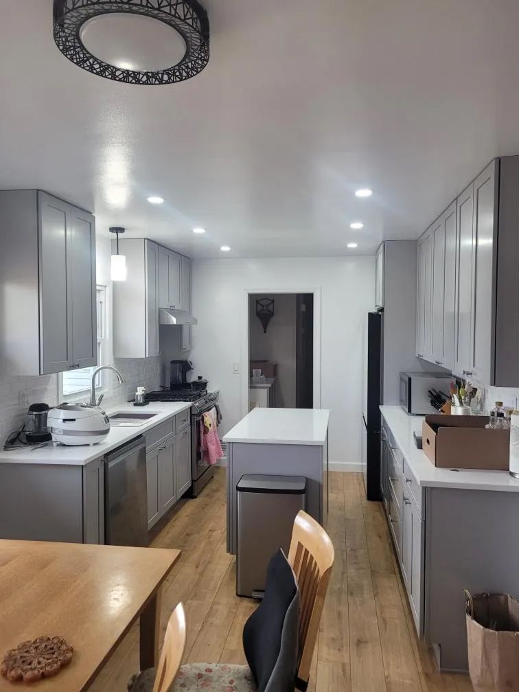 Modern kitchen with gray cabinets, white island, wood floors, and recessed ceiling lights